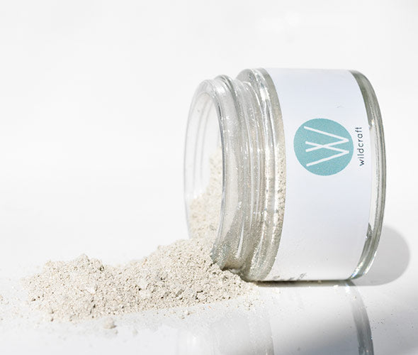 Open jar of Detox Face Mask with some powder spilling on a marbled surface. 