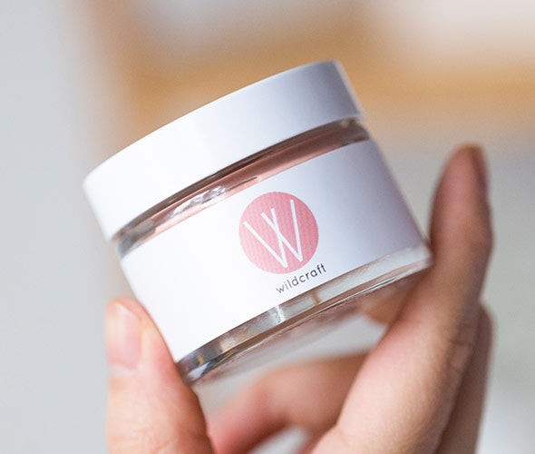 A hand holding a closer jar of Nourish Face Cream